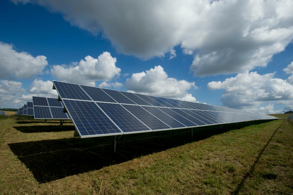 Field with solar panels underneath a sunny but cloudy sky